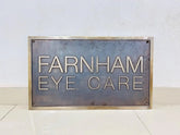 Metal sign with 'Farnham Eye Care' text on a white background
